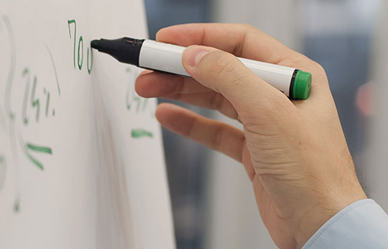 Photo of a hand writing on a whiteboard with a green dry-erase marker