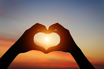 Hands forming the shape of a heart with the sunset in the background