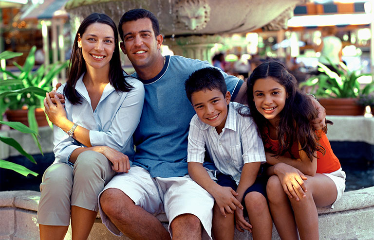 Photo of a family of four sitting on the side of a water fountain