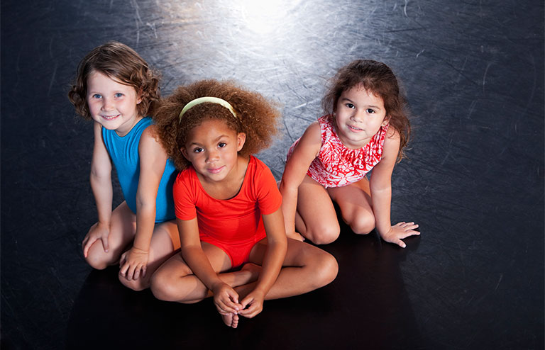 Photo of three young gymnasts sitting on a black mat