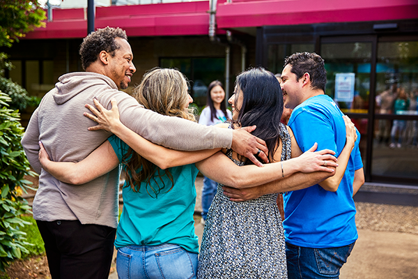 Photo of the backside of four adults holding each other over the shoulders